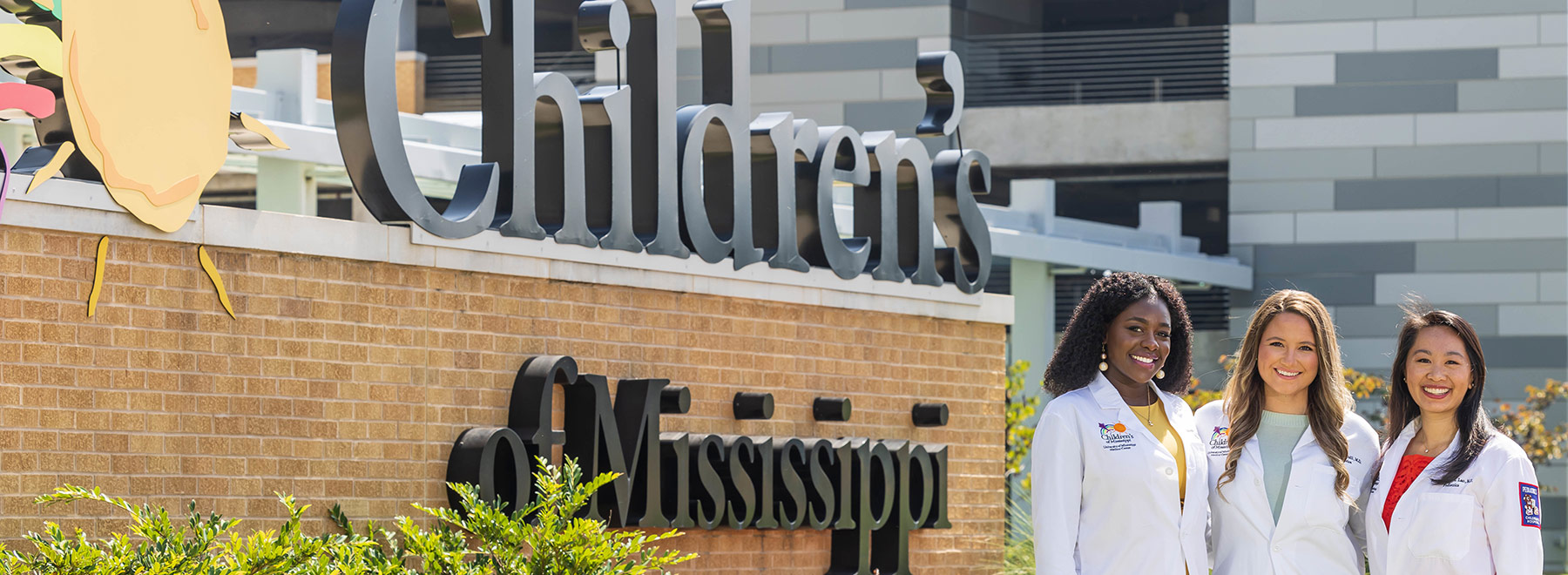 File: 2023 Pediatrics chief residents Elizabeth Adeyemi, India Hemphill, and Breanna Belle Lao standing to the right of the Children's of Mississippi marquee in from of Sanderson Tower.